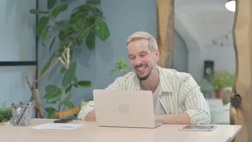 Smiling Young Adult Working on Laptop at Desk