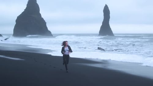 Gloomy Icelandic beach landscape with woman running. Aerial flying backwards