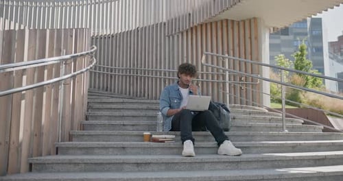 Jeune bel homme indien hindou étudiant indépendant assis à l'extérieur sur des marches à l'aide d'un ordinateur portable