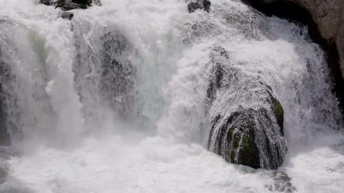 Man sieht einen weiten Blick auf einen kleinen Wasserfall, der große Felsen hinunterfließt.