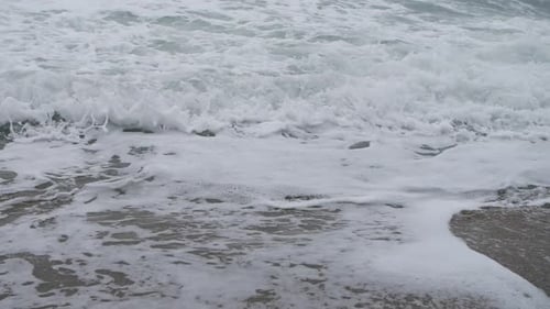 Turbulent foamy waves in slow motion reaching their end of life on the beach.