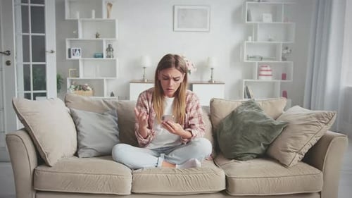 Upset Woman Using Smartphone on Couch Indoors