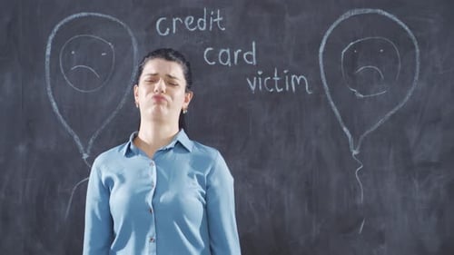The woman who writes Credit card victim on the blackboard looks up with a sad expression.