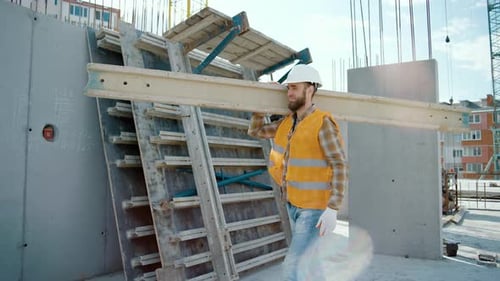 Sliding view of worker carrying long heavy beam. Frame house site building
