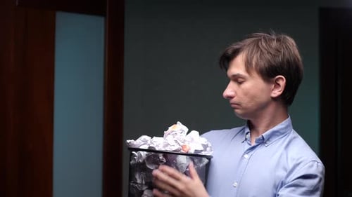 Office Worker Looking at a Wastebasket Full of Crumpled Paper