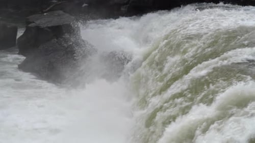Large river flowing over a waterfall onto stone boulders. Slow motion clip.