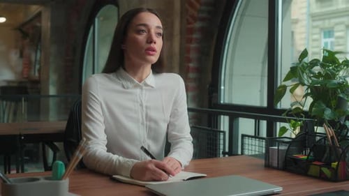 Thoughtful Woman Writing at Desk in Office