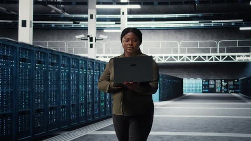 Smiling Engineer Walking in Data Center with Laptop Checking Hardware