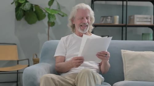 Senior Man Reads Good News on Couch, Thumbs Up