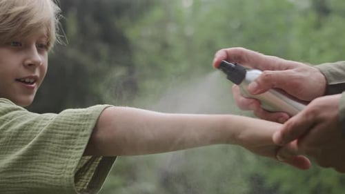 Dad Spraying Insect Repellent on Sons Skin in Forest