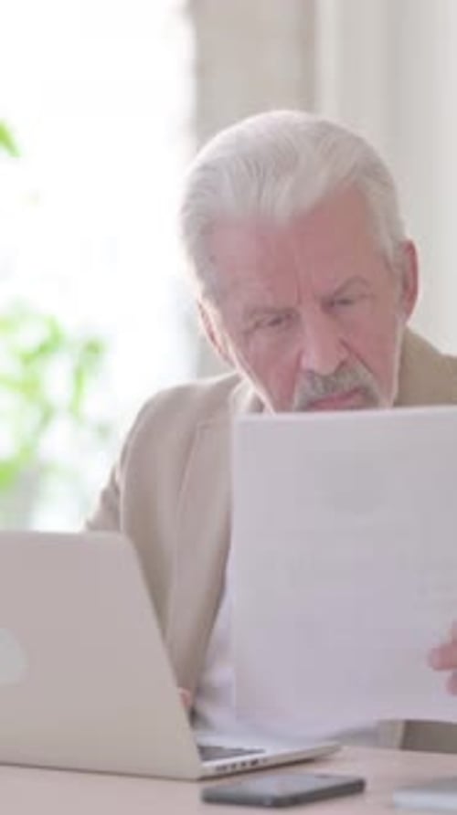Paperwork by Old Man Working on Laptop in Office, Vertical Video