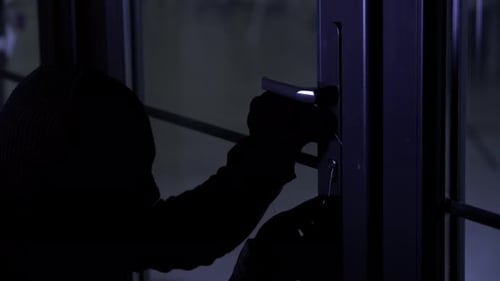 Diebstahl: Männlicher Krimineller in Sturmhaube mit Hauptschlüssel in der Hand öffnet Türschloss in Nahaufnahme