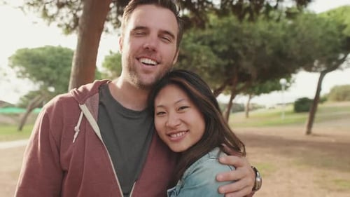 Close up, laughing couple hugging each other while standing in the park