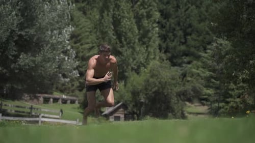 Young caucasian fit attractive male sprinter running exercising outdoors with green vegetation backg