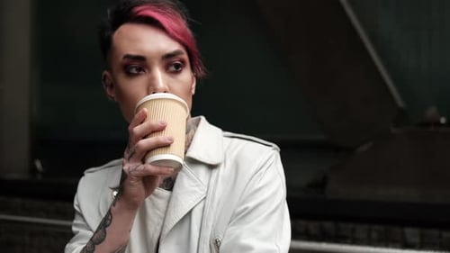 Modelo andrógina apoyada en la pared y tomando café.