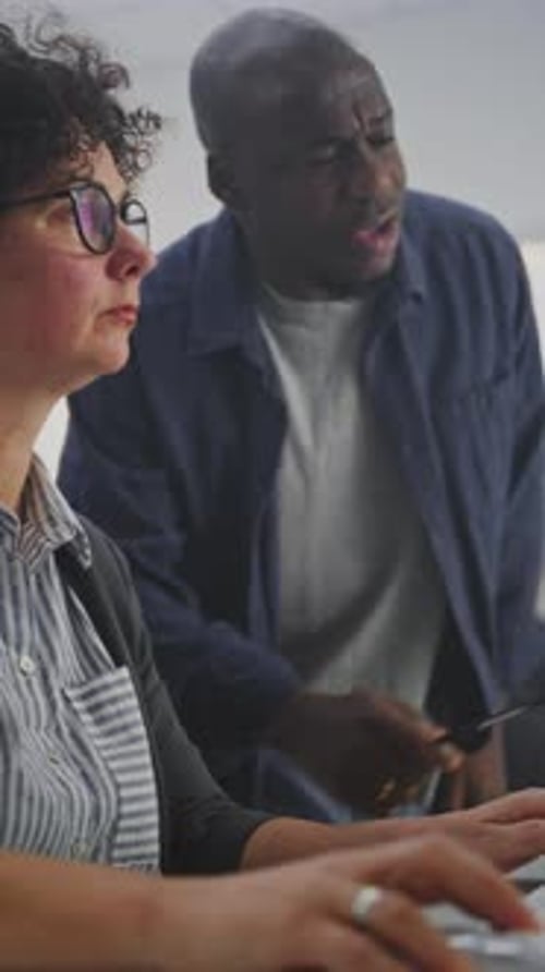 Attentive Instructor Walks Between Adult Students During Programming Workshop in Computer Classroom