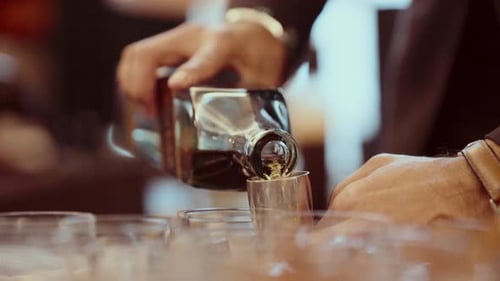 Des mains expertes versent du whisky dans un doseur en métal