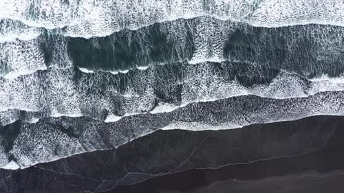 Slow motion aerial view of the Atlantic ocean waves washing volcanic black sandy beach in Iceland