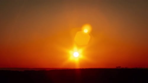 Fantastischer Sonnenuntergang im Zeitraffer mit Linsenreflexlicht, das sich am klaren, orangefarbenen Himmel bewegt