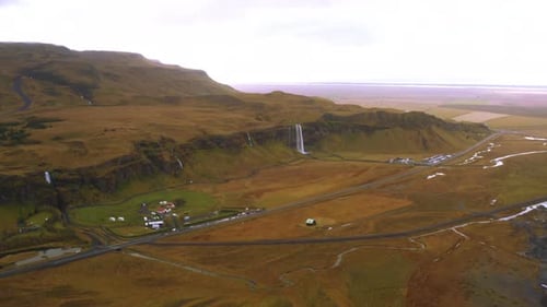 Wide aerial mountain waterfall landscape in Iceland, beautiful green plain and a small village near