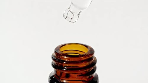 Dropper Dispensing Clear Liquid into Amber Glass Bottle