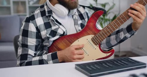 Close up of caucasian young bearded man with headphones having online electric guitar class at home