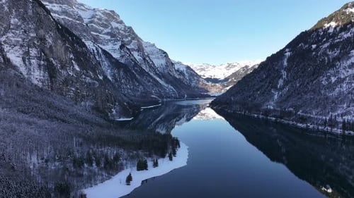Mountain lake Klöntalersee surrounded by snow-capped mountains from an aerial view in winter.