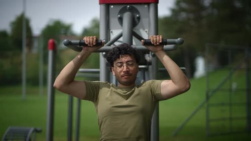 A Man Engaging in Exercise Outdoors on Fitness Equipment Located in a Local Park Setting