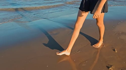 View of Female Legs Walking on the Beach in the Water Water Splashes and Foam From the Waves Washing