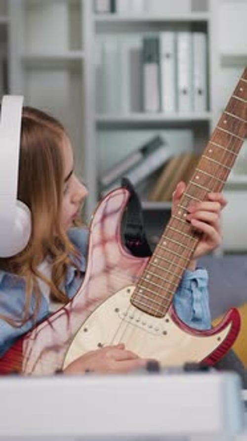 Girl plays electric guitar wearing headphones indoors