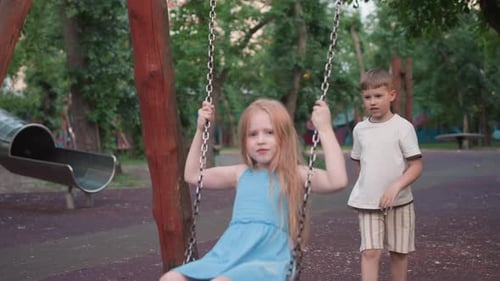 Young Girl on Swing As Playmate Pushes in Evening Park