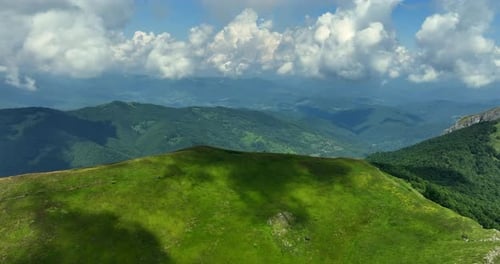Flight over green mountain peaks. A beautiful sunny summer day at high altitude with thick clouds an