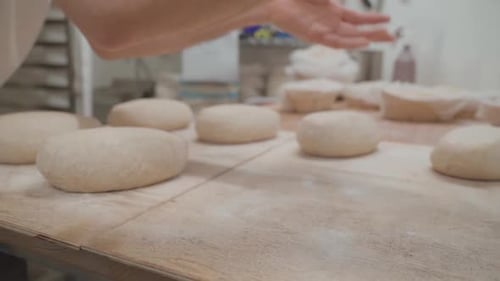 Bread production in bakery. Hands of a baker place portions of raw dough on a table to bake them