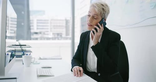 4k video footage of a mature businesswoman writing notes while talking on a cellphone in an office