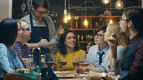 In the Bar/ Restaurant Waiter Takes Order From a Diverse Group of Friends. Beautiful People Drink W