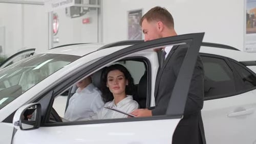 Young Attractive Brunette Woman Sits Behind the Wheel of a New Car in a Car Showroom