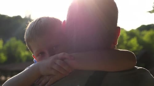 Boy Affectionately Hugging Adult Outdoors in Sunlight