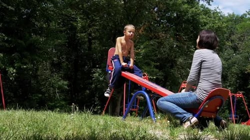 Happy Child Boy and His Mother Swinging on a Street Counterweight Swing at Playground in Slow Motion