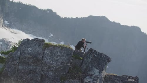 Photographer looks through camera viewfinder with telephoto lens on mountain ridge, Tim Durkan wide