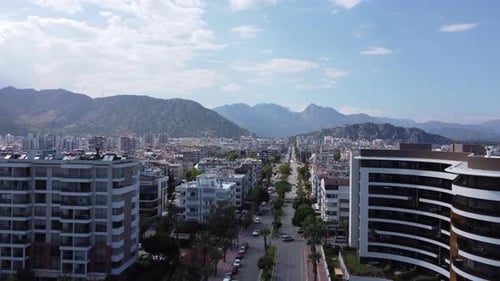 Stunning view of rugged mountain ranges, modern buildings and a long tree-lined avenue