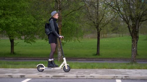Woman Riding Electric Scooter on City Sidewalk