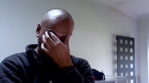 Man in a dark shirt feeling stressed with his hand on his forehead in an office setting, shallow foc