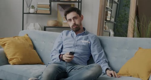 Portrait of Attractive Young Man in Trendy Clothing Watching TV Using Remote Control Relaxing on