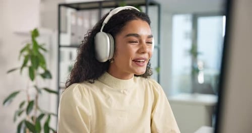 Young Woman Speaking At Desk In Office With Headphones