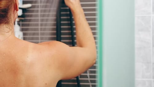 Water Flowing Down Woman’s Back in Shower with Stream Visible and Hair Tied Up, Partial Rear View Th