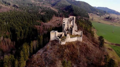 Drone flying backwards revealing the ruins of an ancient medieval castle on an idyllic mountainous e