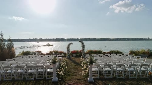 Wide Aerial Drone View of the Outdoor Wedding Setup with Rows of White Chairs Facing a Flower Arch