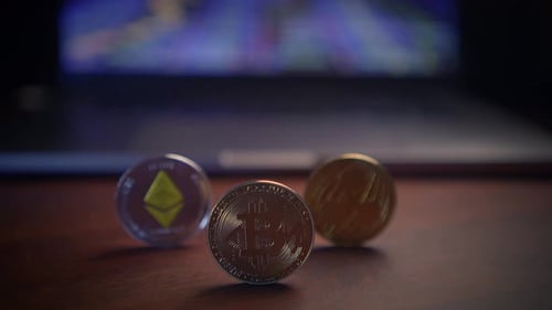 Various Cryptocurrency Coins Displayed on a Table with a Laptop Present in the Background