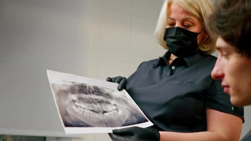 Nahaufnahme der Zahnarztpraxis Blonde Zahnärztin in einer schwarzen Uniform, die einen Patienten berät, zeigt ein Foto des