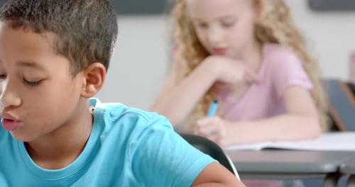 Das kaukasische Mädchen mit lockigem blondem Haar konzentriert sich auf das Schreiben in einem Klassenzimmer in der Schule